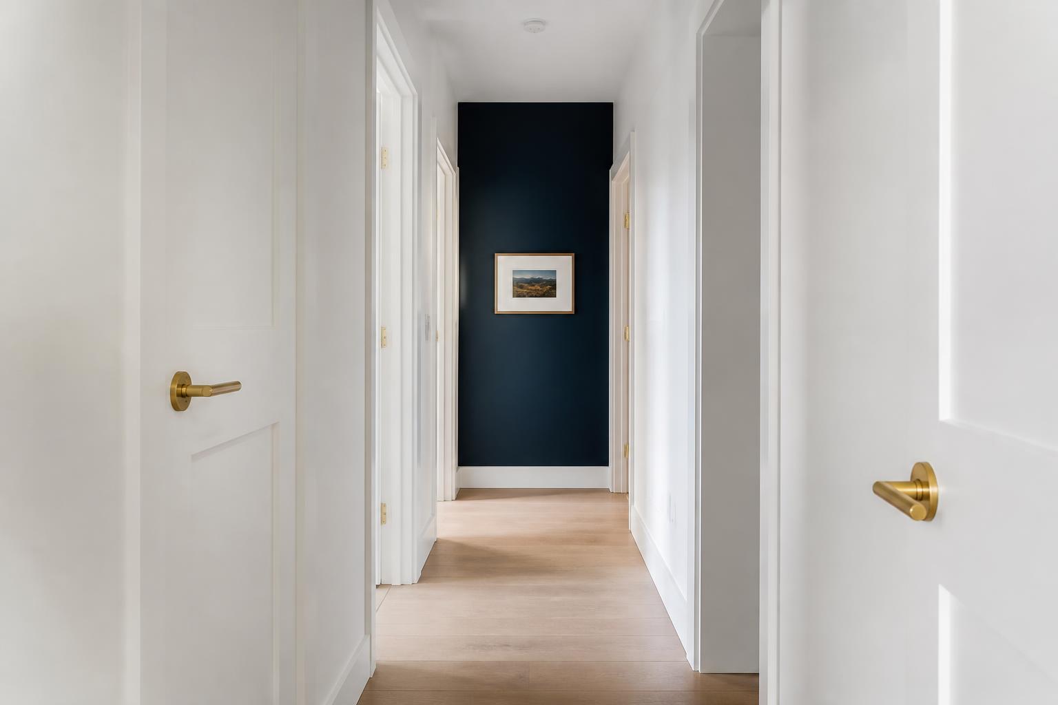 Bright hallway with aligned white doors, a navy accent wall and brushed-gold handles